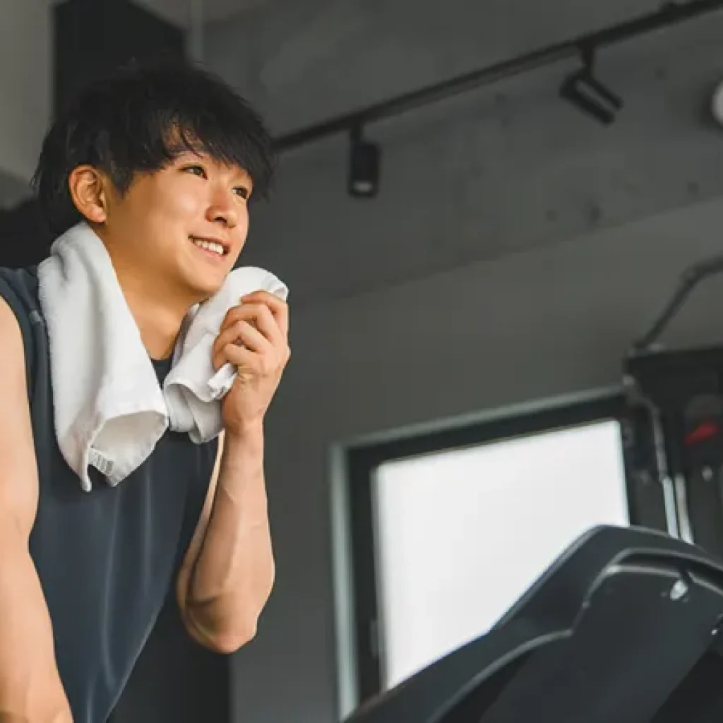 Man wipes face with towel as he works out on a treadmill machine.